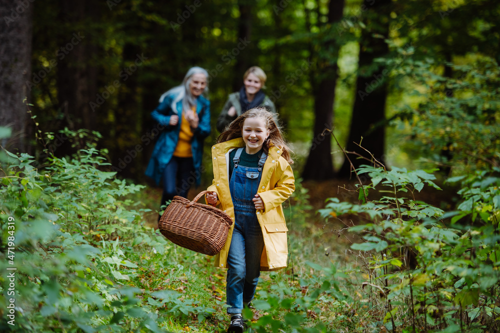 Happy little girl with basket running during walk with mother and grandmother outdoors in forest