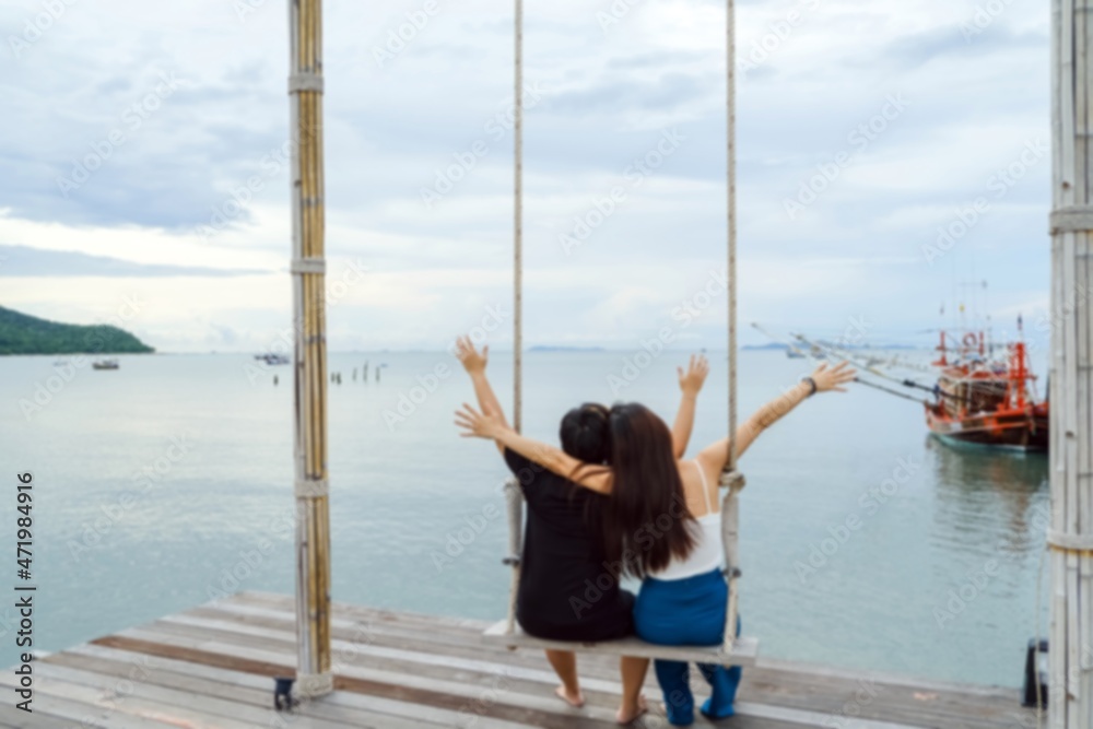 blurred of back view of two asian women having fun together on seaside