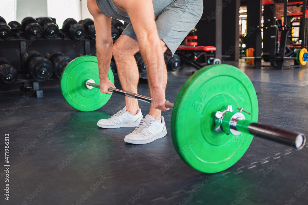 Barbell squats. Man trains in the gym, lifting a barbell. Close up. The concept of fitness and wellness Barbell squats. Man trains in the gym, lifting a barbell. Close up. The concept of fitness and wellness