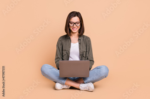 Photo of cheerful positive programmer lady sit floor hold pc wear eyewear khaki shirt isolated beige color background