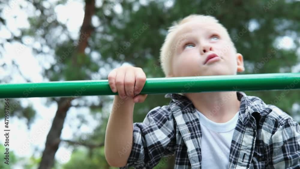 portrait cute blond hair boy with blue eyes playing on playground. children climbs up in the playground in park at sunset. happy family dream kid concept. slow motion portrait cute blond hair boy with blue eyes playing on playground. children climbs up in the playground in park at sunset. happy family dream kid concept. slow motion