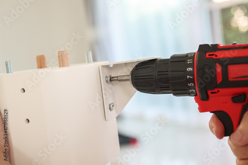 man assembling white table furniture at home using cordless screwdriver