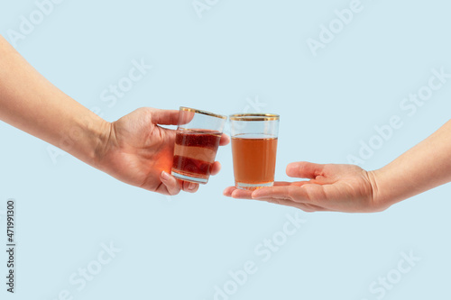 Raise your glass. A celebration where two people toast with a red drink on a pastel blue background. Minimal composition. Toast, cheers. clinking wine glasses