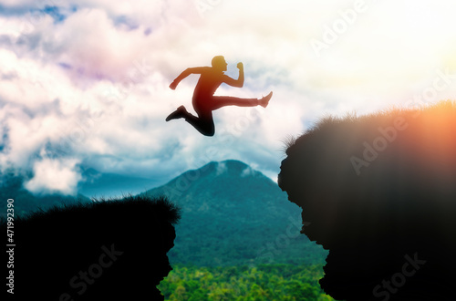 The silhouette of a man jumping over a chasm between rocks. In the background, the ocean and the sky. The concept of freedom, success and overcoming obstacles photo
