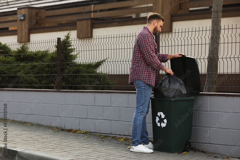 Man putting garbage bag into recycling bin outdoors
