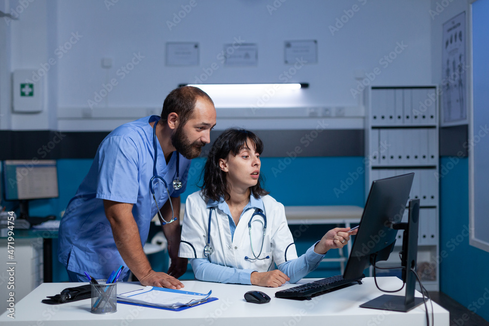 Medical team looking at computer screen for checkup information, working late. Woman working as doctor and assistant using monitor with technology for prescription medicine and healthcare Medical team looking at computer screen for checkup information, working late. Woman working as doctor and assistant using monitor with technology for prescription medicine and healthcare