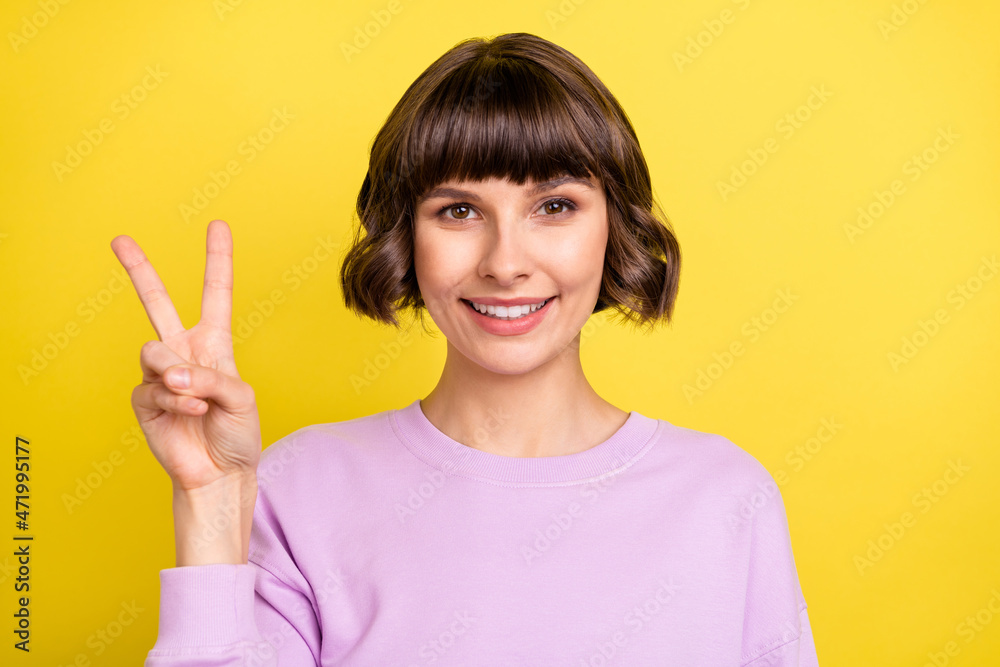 Portrait of attractive cheerful brown-haired girl showing v-sign good mood isolated over bright yellow color background Portrait of attractive cheerful brown-haired girl showing v-sign good mood isolated over bright yellow color background