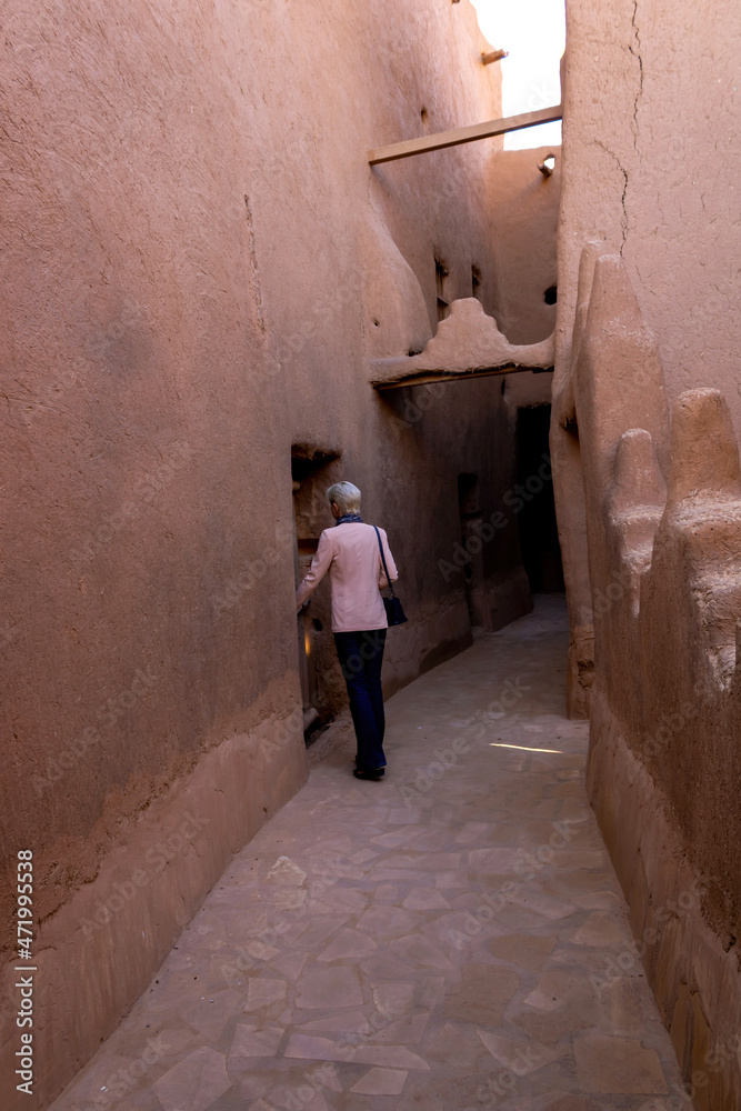 A lonely Western female tourist standing in the narrow street in Ushaiqer Heritage Village, Saudi Arabia. Back view.