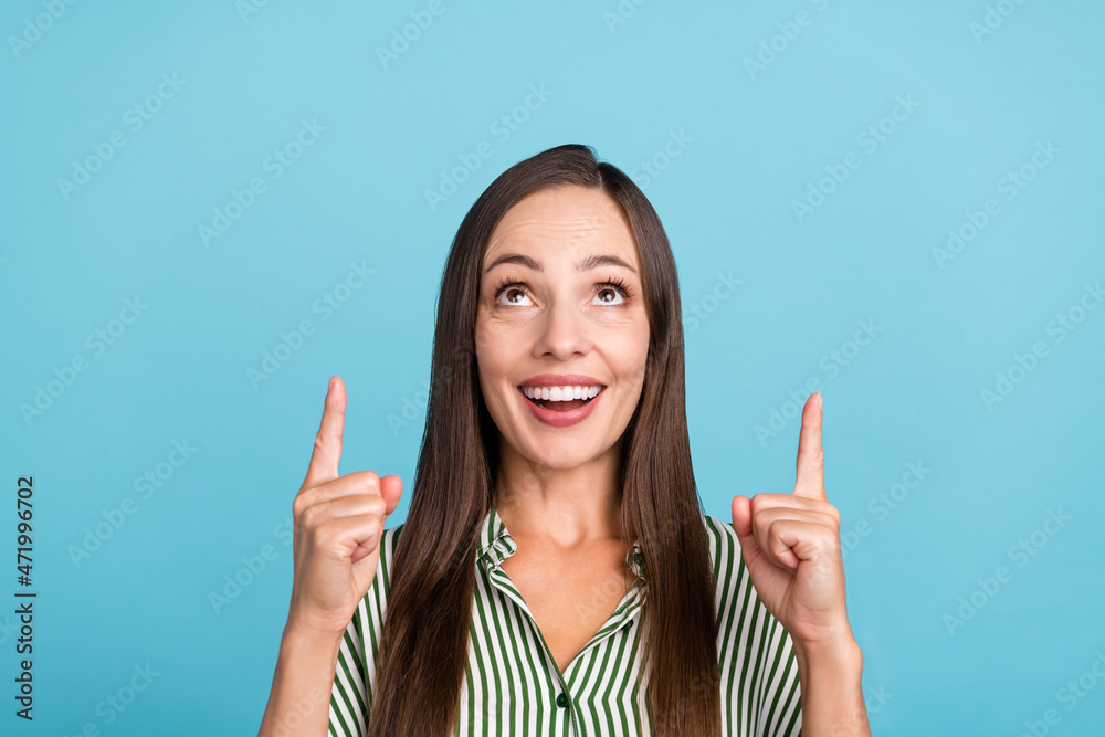 Photo of cheerful young lady look indicate fingers empty space recommend suggest advert isolated over blue color background Photo of cheerful young lady look indicate fingers empty space recommend suggest advert isolated over blue color background