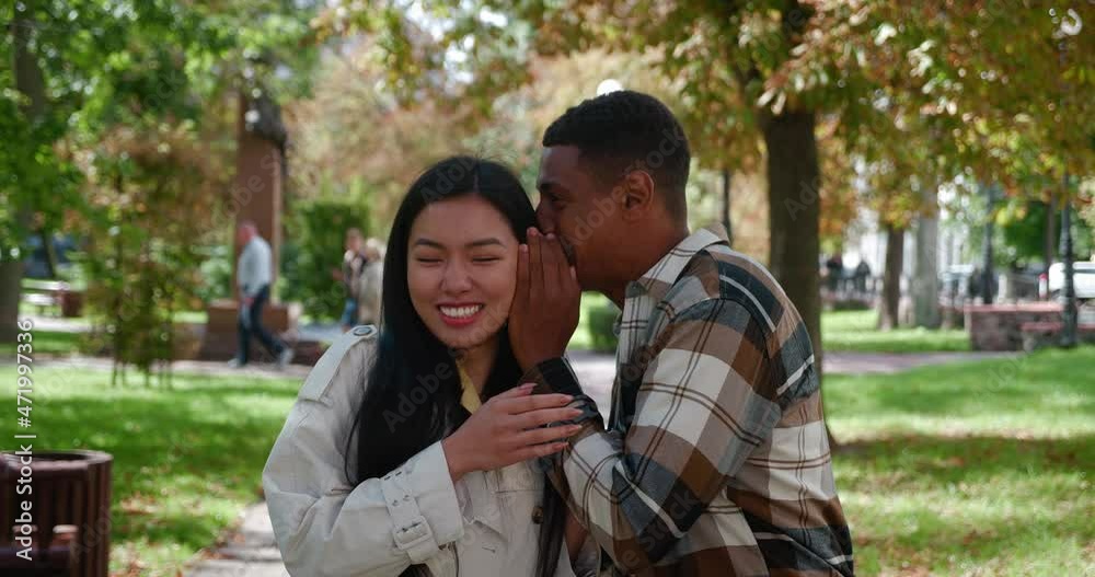 Romantic multi-ethnic couple in love having fun together, laughing, whispering, gossiping, discussing, standing next to each other in a city city park during a romantic date Romantic multi-ethnic couple in love having fun together, laughing, whispering, gossiping, discussing, standing next to each other in a city city park during a romantic date