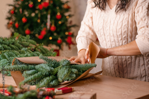 The process of making a winter bouquet of fir branches at home, packaging in kraft paper,close-up of the woman's hands.New Year, Christmas and eco-friendly concept.Selective focus.