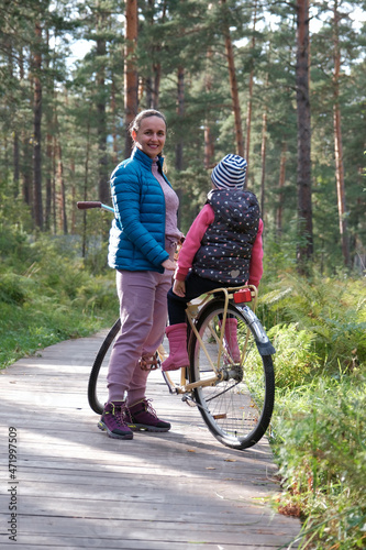 Young Sporty Mother and Little Daughter with Bicycle on the Wooden Path in a Forest

