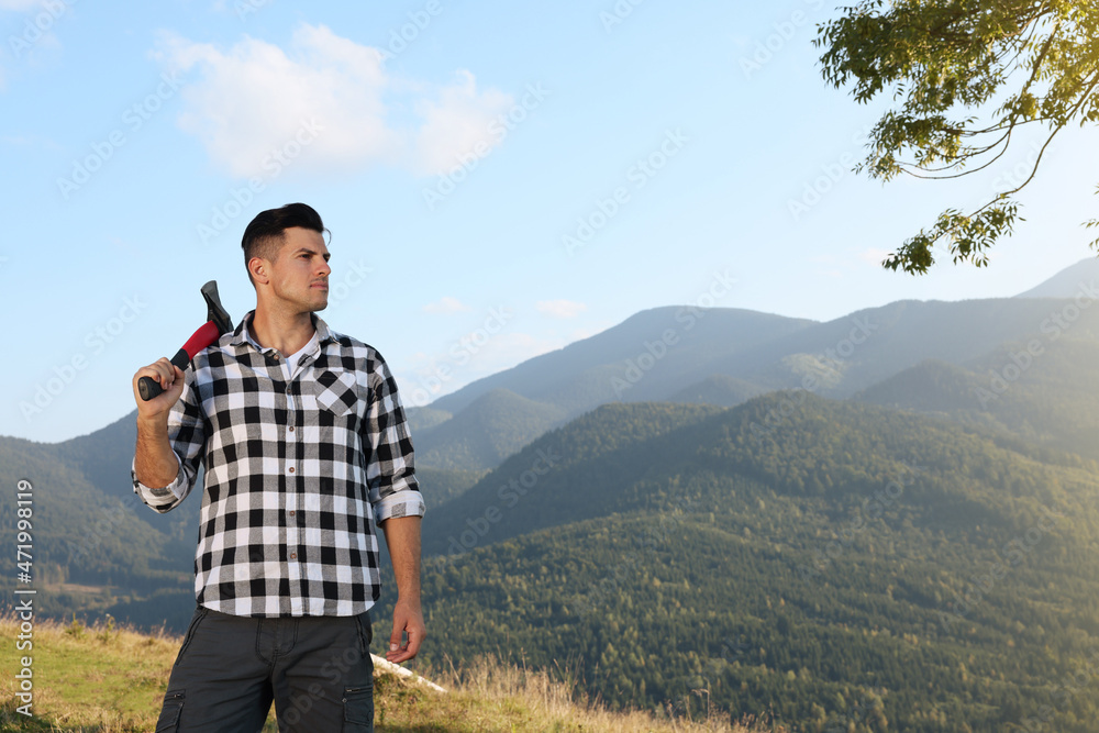 Handsome man with axe in mountains, space for text Handsome man with axe in mountains, space for text