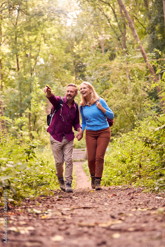 Mature Loving Couple In Countryside Hiking Along Path Through Forest Together Holding Hands