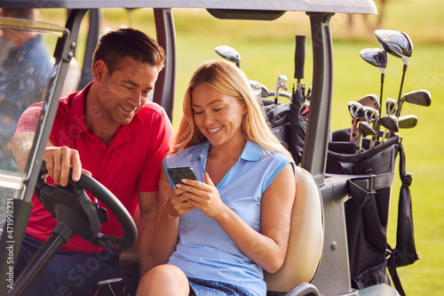 Couple Sitting In Golf Buggy On Course With Woman Using Mobile Phone