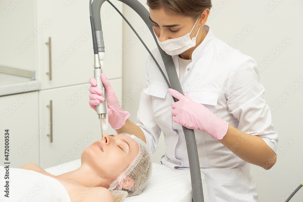Naklejka premium Doctor cosmetologist makes a laser dermal rejuvenation procedure to a patient. Against the background of a medical office with copy space.
