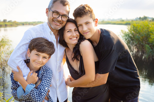 happy family, mother, father and two cheerful children hugging in nature