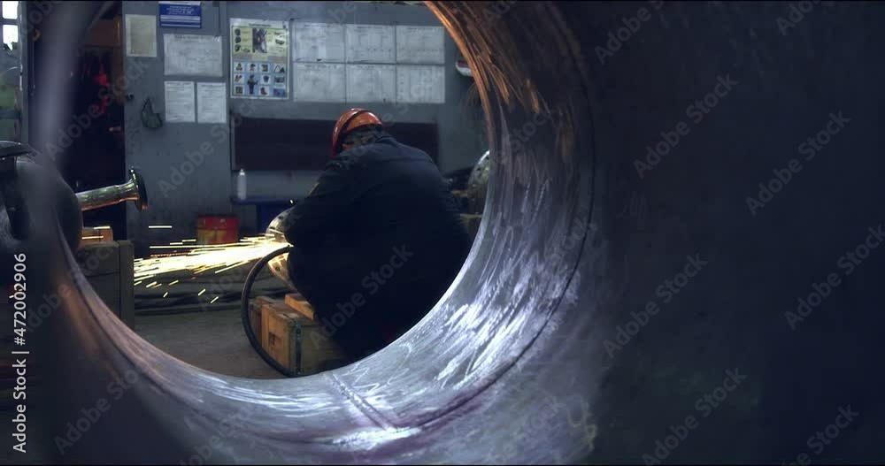 A professional worker in a protective mask and uniform works with a grinding machine for smoothing steel in a factory. Production of heavy industry and large metal structures. Modern steel industry.