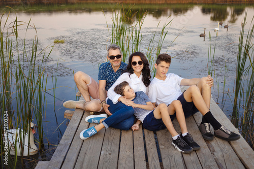 Happy family sitting on a pier on a lake or pond, relaxing in nature