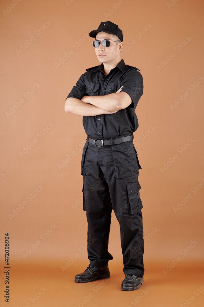 Retail store security guard officer in black uniform standing with arms folded Retail store security guard officer in black uniform standing with arms folded