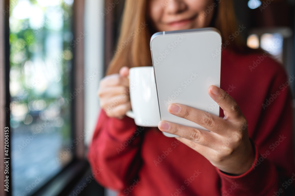 Closeup of a young woman holding and using mobile phone while drinking coffee in cafe Closeup of a young woman holding and using mobile phone while drinking coffee in cafe