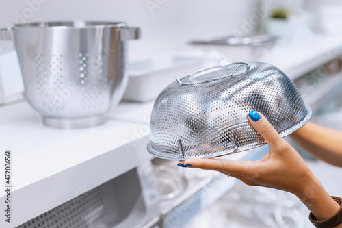 The housewife holds in her hands and chooses a metal colander for cooking pasta in the store
