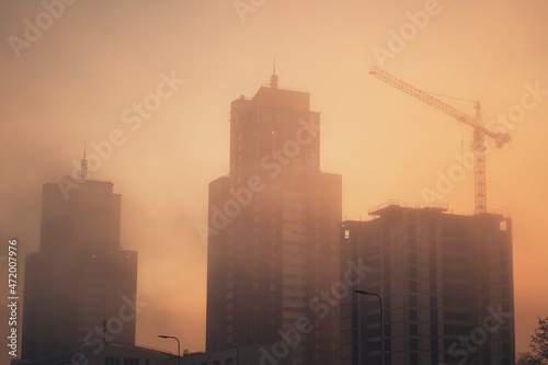 Silhouette of a construction crane and unfinished residential building on a foggy autumn morning during the sunrise. Housing construction, apartment block