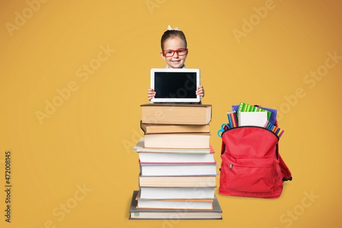 Smiling caucasian school child sitting behind the stack of book shows the tablet