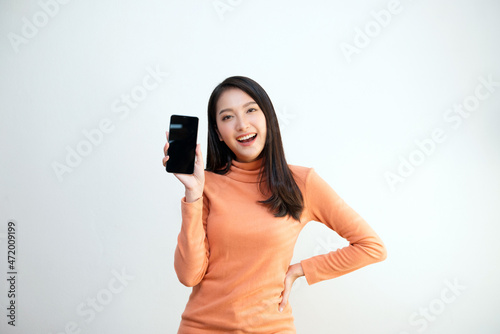 Attractive Asian girl portrait, wearing orange shirt, holding smartphone, smiling face, showing emotion, for communication, advertisement, copy space.