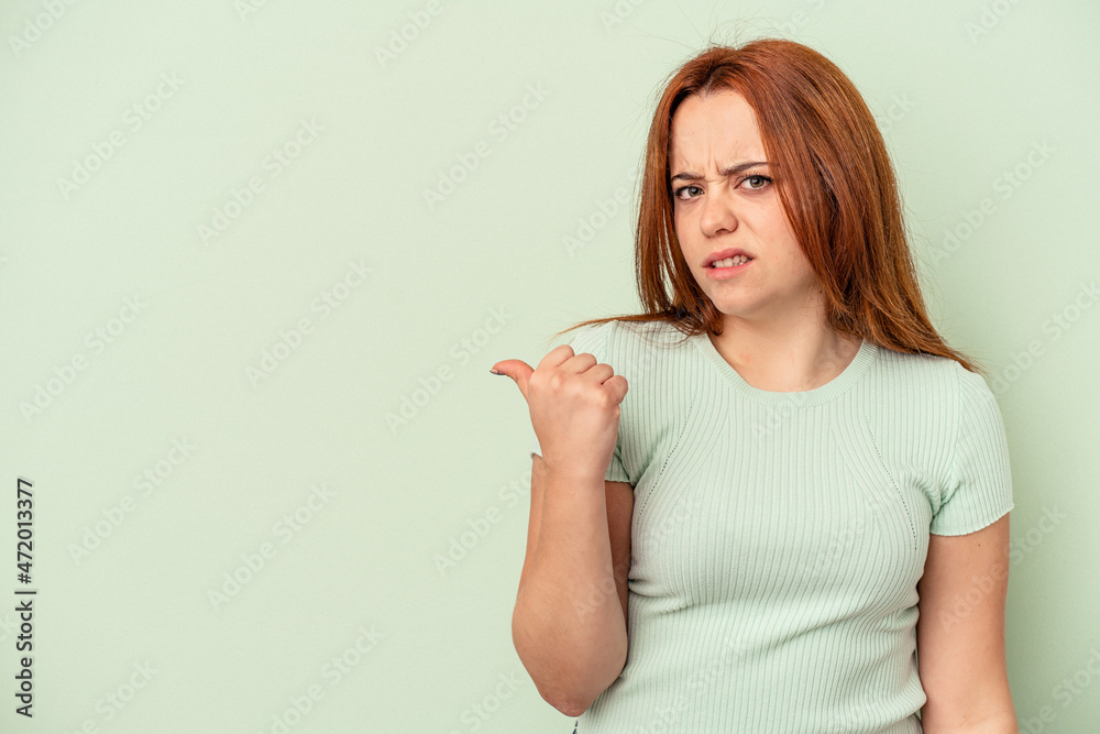 Young caucasian woman isolated on green background shocked pointing with index fingers to a copy space. Young caucasian woman isolated on green background shocked pointing with index fingers to a copy space.