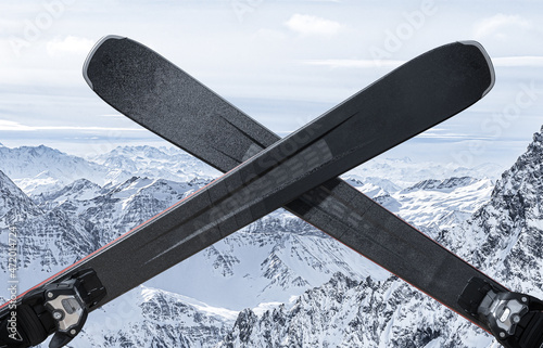 closure of ski resort or ski season. Black alpine skis are crossed. snow mountains in background. close of ski resorts, end of season