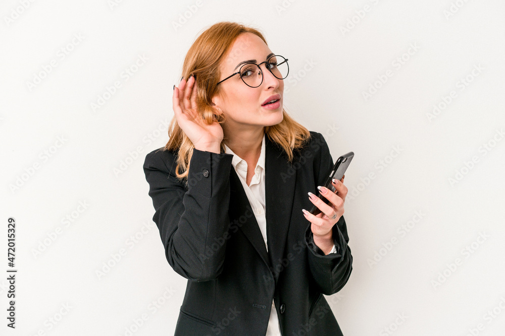 Young business caucasian woman holding mobile phone isolated on white background trying to listening a gossip.