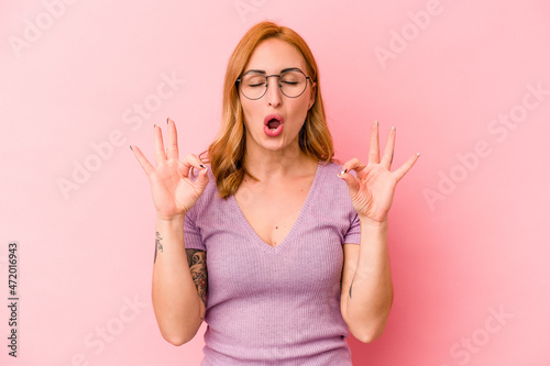 Young caucasian woman isolated on pink background relaxes after hard working day, she is performing yoga. © Asier