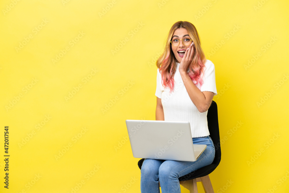 Naklejka premium Young woman sitting on a chair with laptop over isolated yellow background with surprise and shocked facial expression