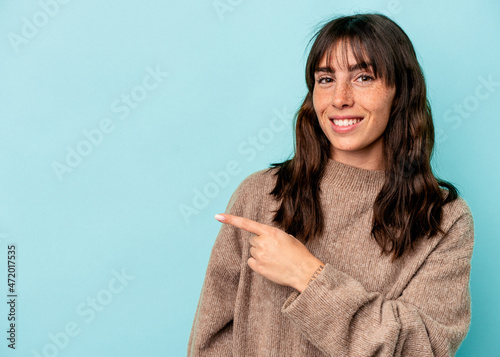 Young Argentinian woman isolated on blue background smiling and pointing aside, showing something at blank space.