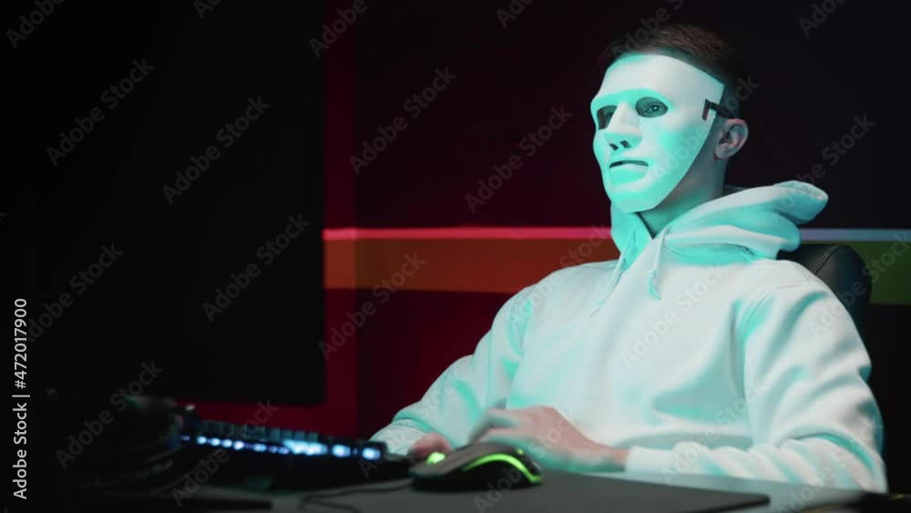 Masked hacker enjoys hacking a database on a computer, hacking in a ...