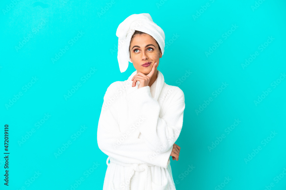 Young woman in a bathrobe over isolated blue background having doubts while looking up Young woman in a bathrobe over isolated blue background having doubts while looking up