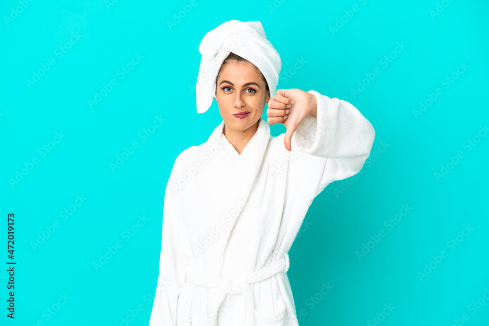 Young woman in a bathrobe over isolated blue background showing thumb down with negative expression Young woman in a bathrobe over isolated blue background showing thumb down with negative expression