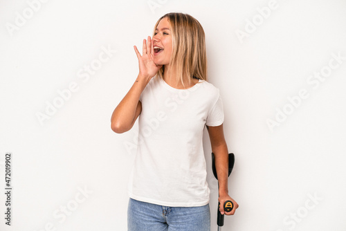 Young caucasian woman holding crutch isolated on white background shouting and holding palm near opened mouth. photo