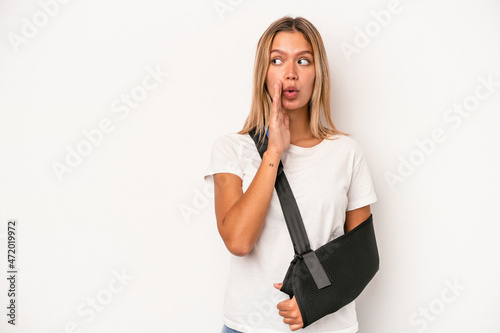 Young caucasian woman with broken hand isolated on white background is saying a secret hot braking news and looking aside