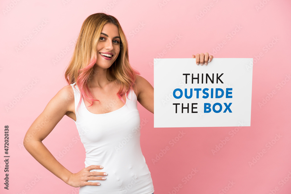 Young woman over isolated pink background holding a placard with text Think Outside The Box with happy expression Young woman over isolated pink background holding a placard with text Think Outside The Box with happy expression