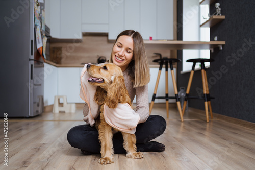 Lovely woman playing with her dog and taking care covering it in a blanket and hugging the pet at home