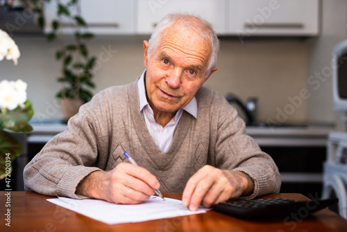 elderly pensioner writing on piece of paper at table in kitchen