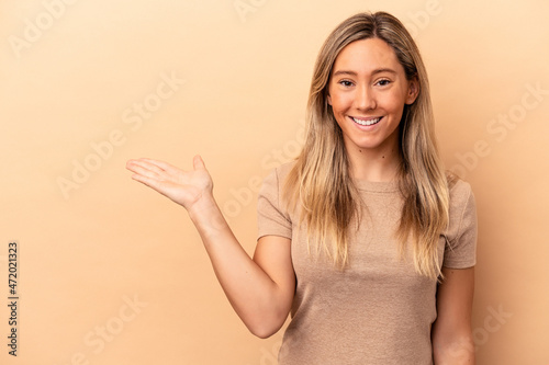 Young caucasian woman isolated on beige background showing a copy space on a palm and holding another hand on waist.