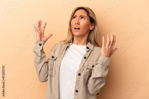 Young caucasian woman isolated on beige background screaming to the sky, looking up, frustrated.