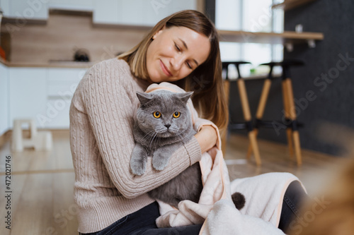 Lovely woman playing with her cat and taking care covering it in a blanket and hugging the pet at home