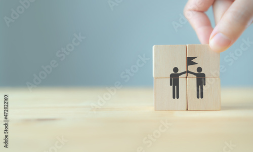 Business success and goal achievement concept with unity and teamwork. Businessman hold wooden cubes with wining team icon on beautiful grey background, copy space. Banner for winner and leader.