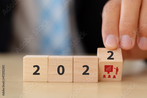 Training and knowledge sharing concept. Workforce and team training plan in 2022. Businessman flips the wooden cubes with 2022 and training symbols on beautiful white background and copy space.