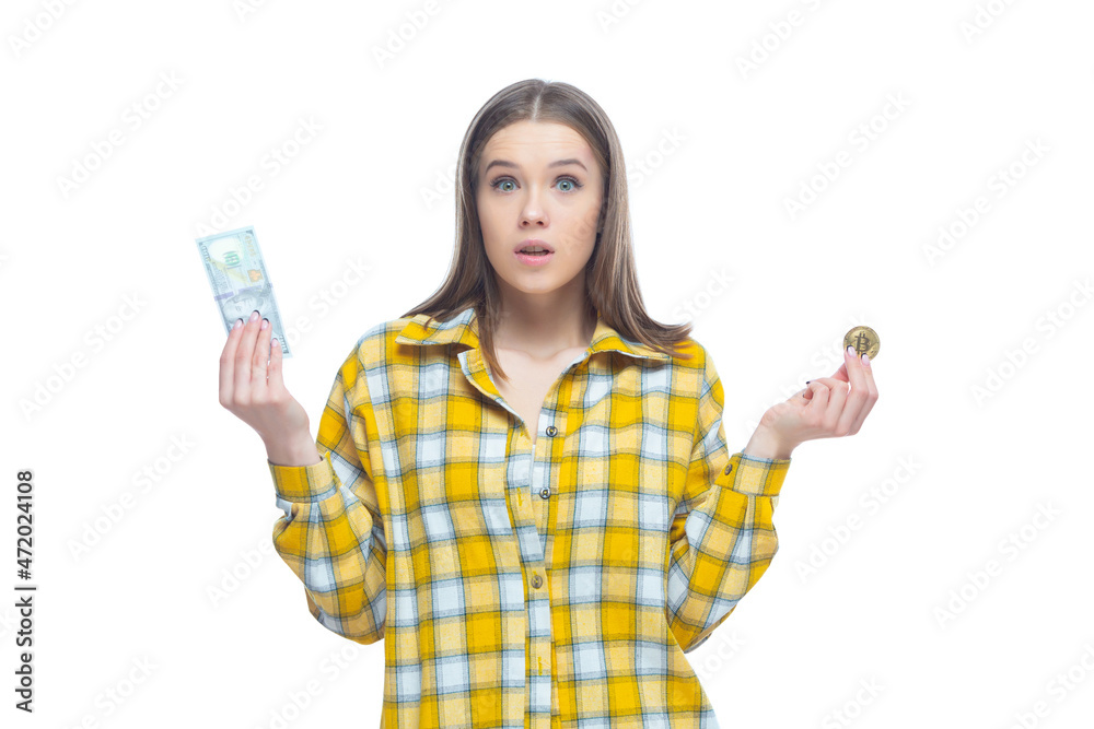 Shot of an astonished young female holding a golden bitcoin in one hand and dollar banknote in the other hand. Doubts where to invest, the choice of currency Shot of an astonished young female holding a golden bitcoin in one hand and dollar banknote in the other hand. Doubts where to invest, the choice of currency