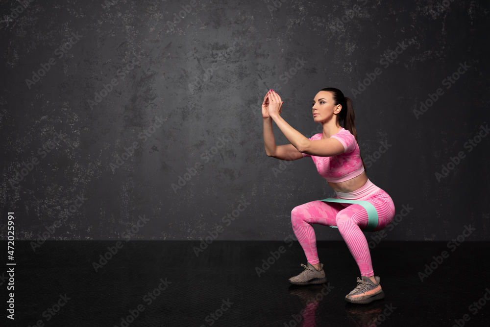 Healthy young fitness woman doing exercises over black background. Exercises with an elastic band. Sports and healthy lifestyle